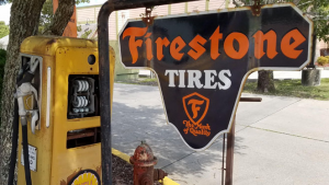 Original Firestone Tires metal sign with antique gas pump located at the left corner of Ross Tire & Service's main entrance